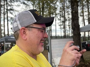 Trevor Shaw in profile at an outdoor festival, laughing, camera in hand.